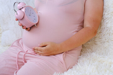 middle-aged pregnant woman holds alarm clock near her belly close-up, waiting for newborn, concept...