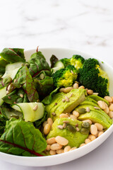 Healthy breakfasts, chard salad with beans and cucumbers, avocado and broccoli sprinkled with different seeds, a plate with food on a white marble background