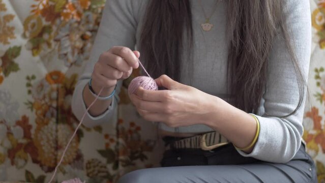 Woman holds back of yarn, wraps up pink yarn from larger spool