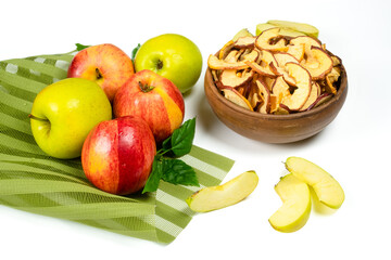 Dry apple slices in a bowl and fresh apples on white background. Dehydrated snacks of apple fruits. Healthy, no sugar sweet food. Candied fruit