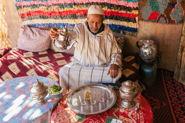 Moroccan man in traditional dress doing ritual preparation of mint tea on outdoor terrace