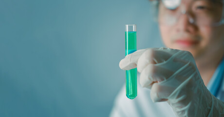 Young asian male scientist hand holds test tubes filled with green chemicals sample for experimental in chemistry science laboratory. Glassware in medical research. Scientific lab for Biotechnology.