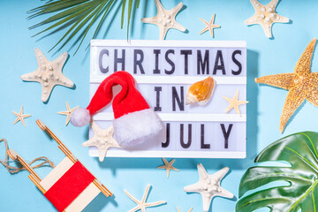 Christmas in July summer holiday or sale background. Summer vacation accessories, seashells, Starfish, lounge chair with Santa hat, tropical leaves. Getaway during winter holiday, top view copy space 