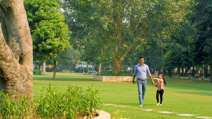 Urban father wearing shirt and jeans enjoying a leisure walk with his daughter. Long shot of a...