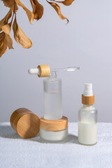 Bamboo cream jar and dropper bottle with face oil on a white towel. Cosmetic container mock-ups. Background for branding and packaging presentation. Natural skincare beauty product concept.