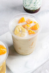 Kolak pisang ubi, kolak biji salak is Indonesian Dessert during Ramadhan made from banana, sweet potato cooked with coconut Milk, palm Sugar. Serving in plastic glass, white background.