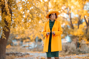 Beautiful woman walks outdoors in autumn. She is wearing a yellow coat, yellow hat and green dress. Young woman enjoying the autumn weather. Autumn content