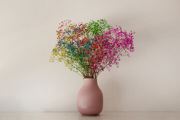 Multicolored flowers in a small pink vase on a white smooth surface