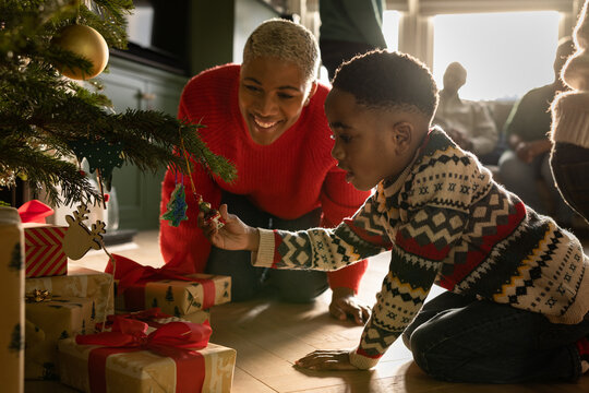 Mother and son looking at Christmas tree decorations with multi generational family celebrating