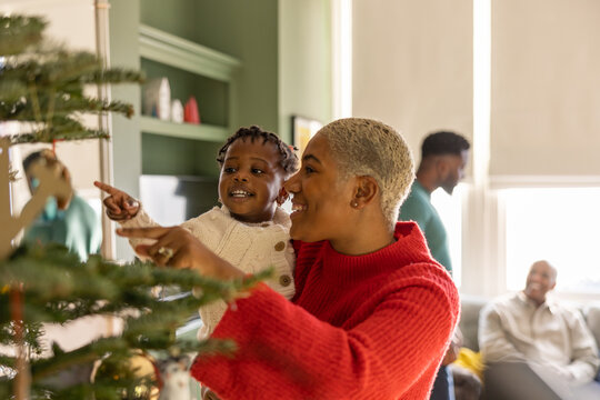 Mother and daughter decorating Christmas tree with multi generational family celebrating