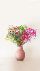 Multicolored flowers in a small pink vase on a white smooth surface