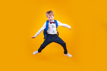 Fototapeta na wymiar Full length shot of a boy with a backpack jumping on yellow background