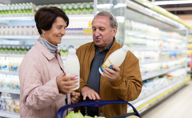 Elderly man and elderly woman choose milk in supermarket