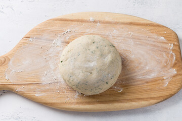 Wooden board with dough for cottage cheese buckwheat flatbread with greens on a light blue background, top view