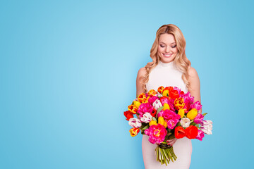 Portrait with copy space empty place of charming pretty woman in white dress having big bouquet of tulips in hands looking at flowers isolated on pink background