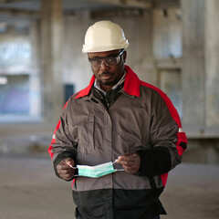 African american builder stands at construction site and holds medical mask