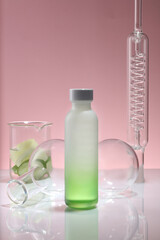 A gradient white and green bottle placed on mirror table with a condenser, a beaker of Cucumber and flasks. Mockup of skin care product extracted from Cucumber (Cucumis sativus)