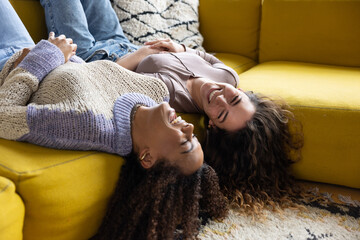 Female friends laughing and hanging down from sofa