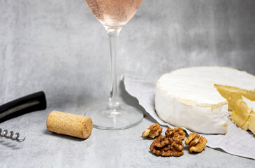 composition from rose wine bottle,glass, round cheese with one cut slice,walnuts,cork and corkscrew on kitchen striped towel or gray background tiles imitation.bottle upside down,flat lay front view