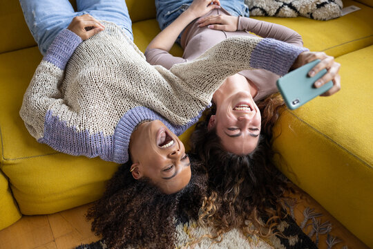 Overhead shot of female friends laughing and taking a fun selfie at home - Powered by Adobe