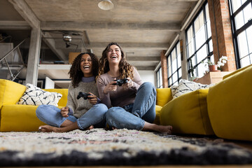 Female friends playing video game sitting on floor in loft apartment