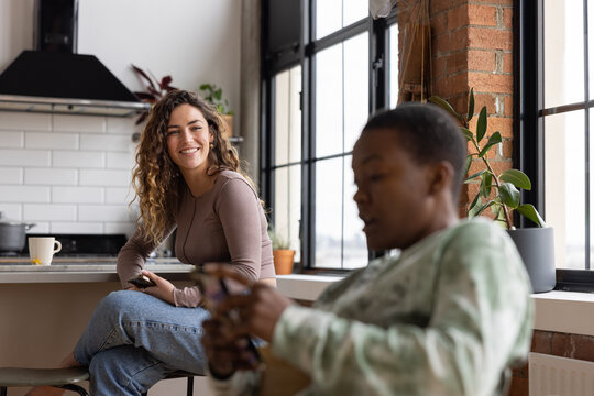 Young adult female sitting in kitchen using a Smartphone in loft apartment with roommates