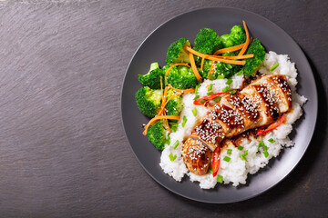 Plate of teriyaki chicken with vegetables and rice on dark background