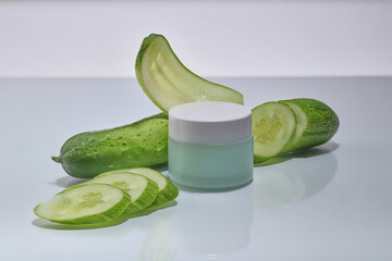 A cosmetic container decorated on minimal white background with several Cucumber slices. Empty label for branding mockup of Cucumber (Cucumis sativus) extract. Natural organic beauty concept
