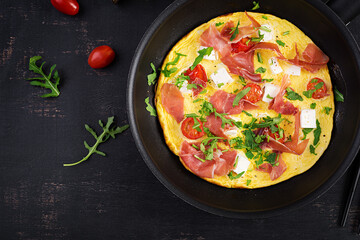 Omelet with tomatoes, jamon and feta cheese in pan. Top view