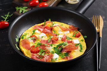 Omelet with tomatoes, jamon and feta cheese in pan.