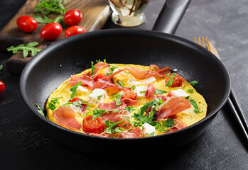 Omelet with tomatoes, jamon and feta cheese in pan.