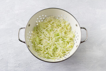 White colander with chopped and steamed cabbage on a light gray background, top view. Cooking vegan healthy food