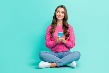 Full length photo of dreamy cute girl wear pink sweater texting twitter telegram facebook empty space isolated turquoise color background