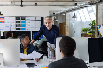 Group of coworkers meeting round a desktop computer in discussion