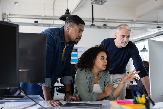 Group of coworkers meeting round a desktop computer in discussion