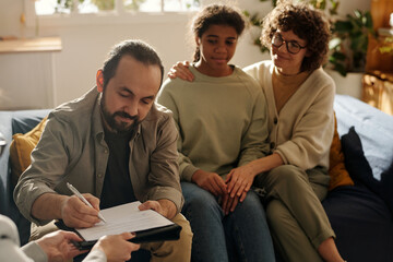 Dad signing custody contract during meeting with social worker with mom and adopted daughter...