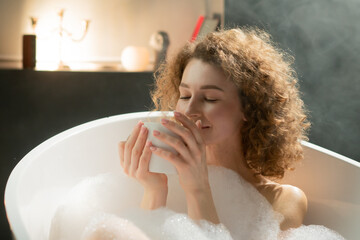 Young relaxed woman lying in the bath enjoys the smell of fragrant tea. Attractive woman lies in a...