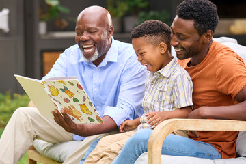 Smiling Multi-Generation Male Family Reading Book In Garden Together