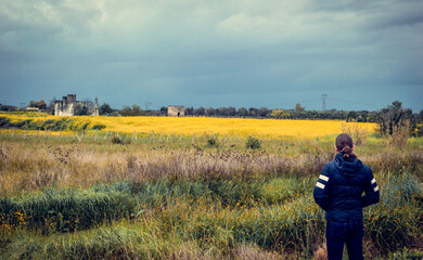 Man standing in a field and watching a country landscape with a yellow flower meadow, mediterranean...
