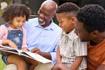 Smiling Multi-Generation Family Reading Book In Garden Together