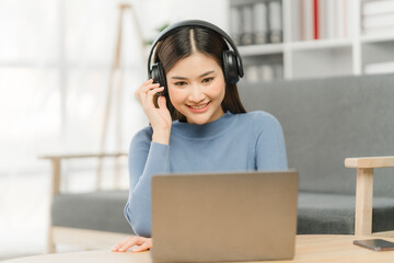 Beautiful smiling young woman in headphones chatting via laptop computer video call at home