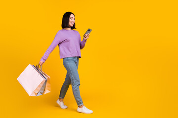 Full length photo of cute shiny lady dressed purple shirt texting gadget holding bargains empty space isolated yellow color background