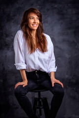 Fototapeta premium Smiling brunette woman wearing blazer and jeans against dark background