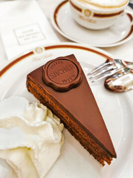 Vienna, Austria &ndash; July 4, 2022: Original chocolate Sacher Cake at Sacher Hotel served with whipped cream in a white plate, cup of coffee and cutlery beside. Top shot, selective focus