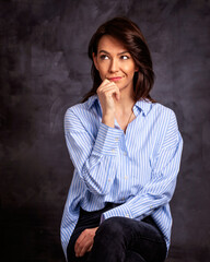 Studio portrait of attractive woman wearing shirt and looking up while sitting at isolated dark background.