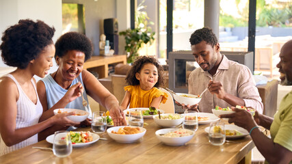 Multi-Generation Family Sitting Around Table Serving Food For Meal At Home 