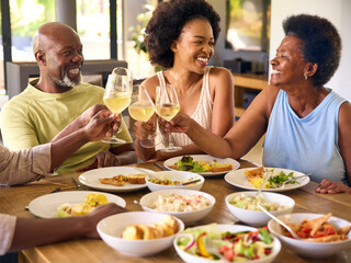 Family Shot With Senior Parents And Adult Offspring Around Table At Home Doing Cheers Before Meal