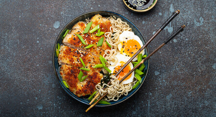 Asian noodles ramen soup with deep fried panko chicken fillet and boiled eggs in ceramic bowl with chop sticks and soy sauce on stone rustic background top view - obrazy, fototapety, plakaty
