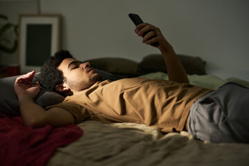 Young man lying on bed without mood and using his smartphone, he staying alone at home