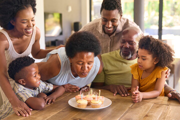 Multi-Generation Family Celebrate Grandmother's Birthday With Cake And Candles Around Table At Home 